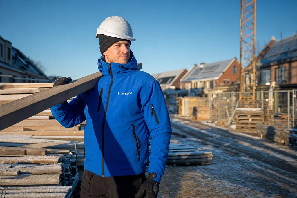 Bouwvakker met helm en winterjas op de bouwplaats onder een strakblauwe winterlucht